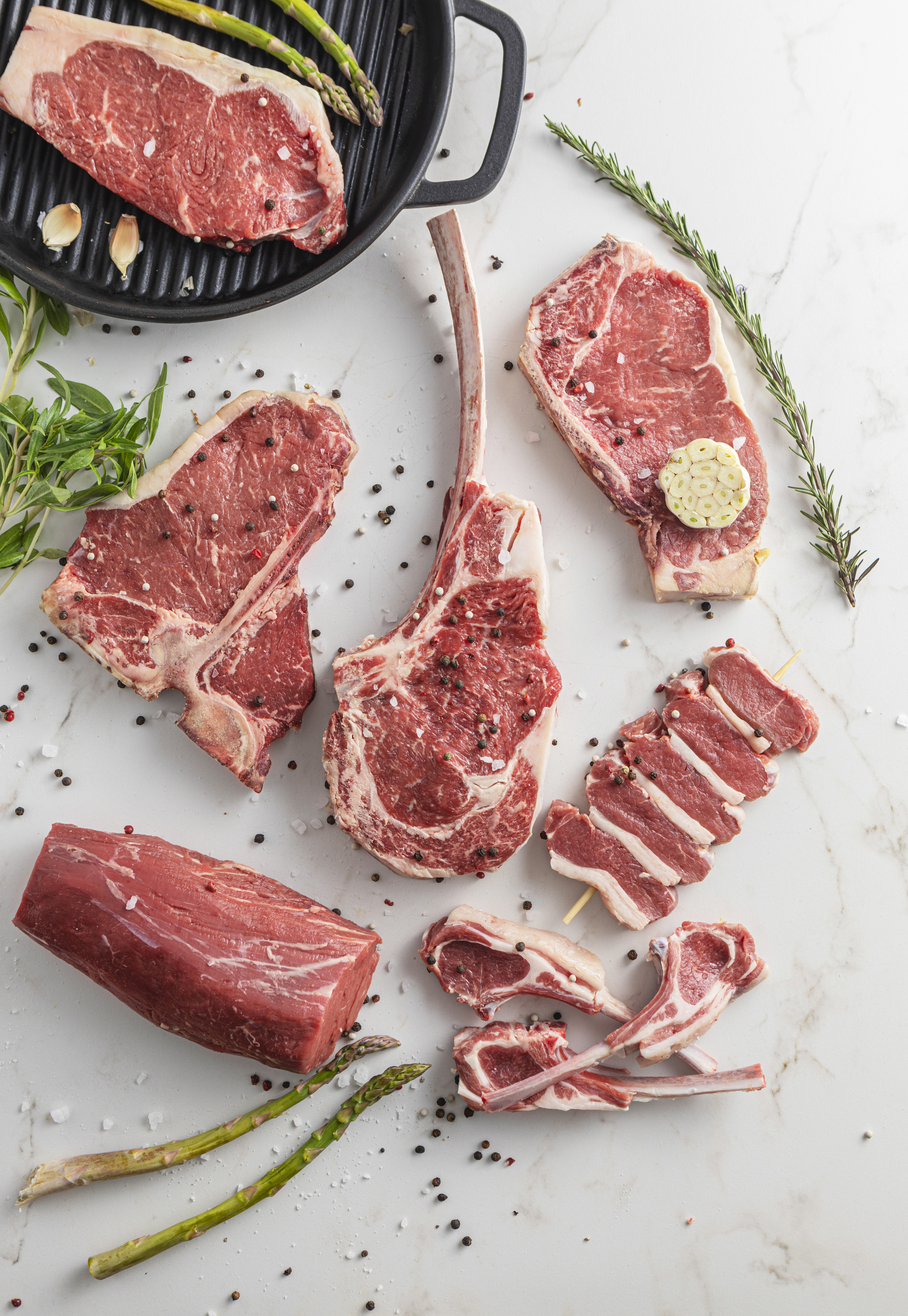 raw beef meat steaks for grilling with seasoning and utensils on marble background 