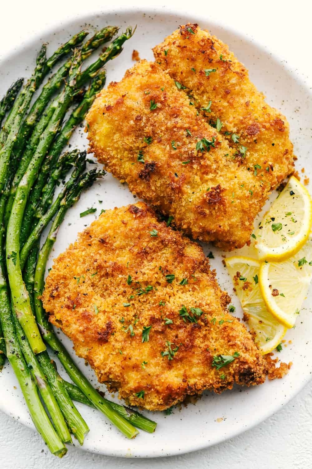 Two pieces of breaded cod with asparagus and lemon slices.