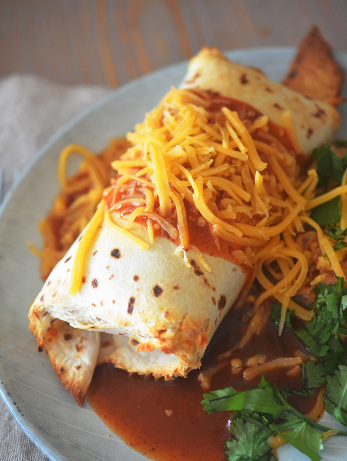 An air fried burrito with a golden brown tortilla covered in red enchilada sauce and shredded cheddar cheese.