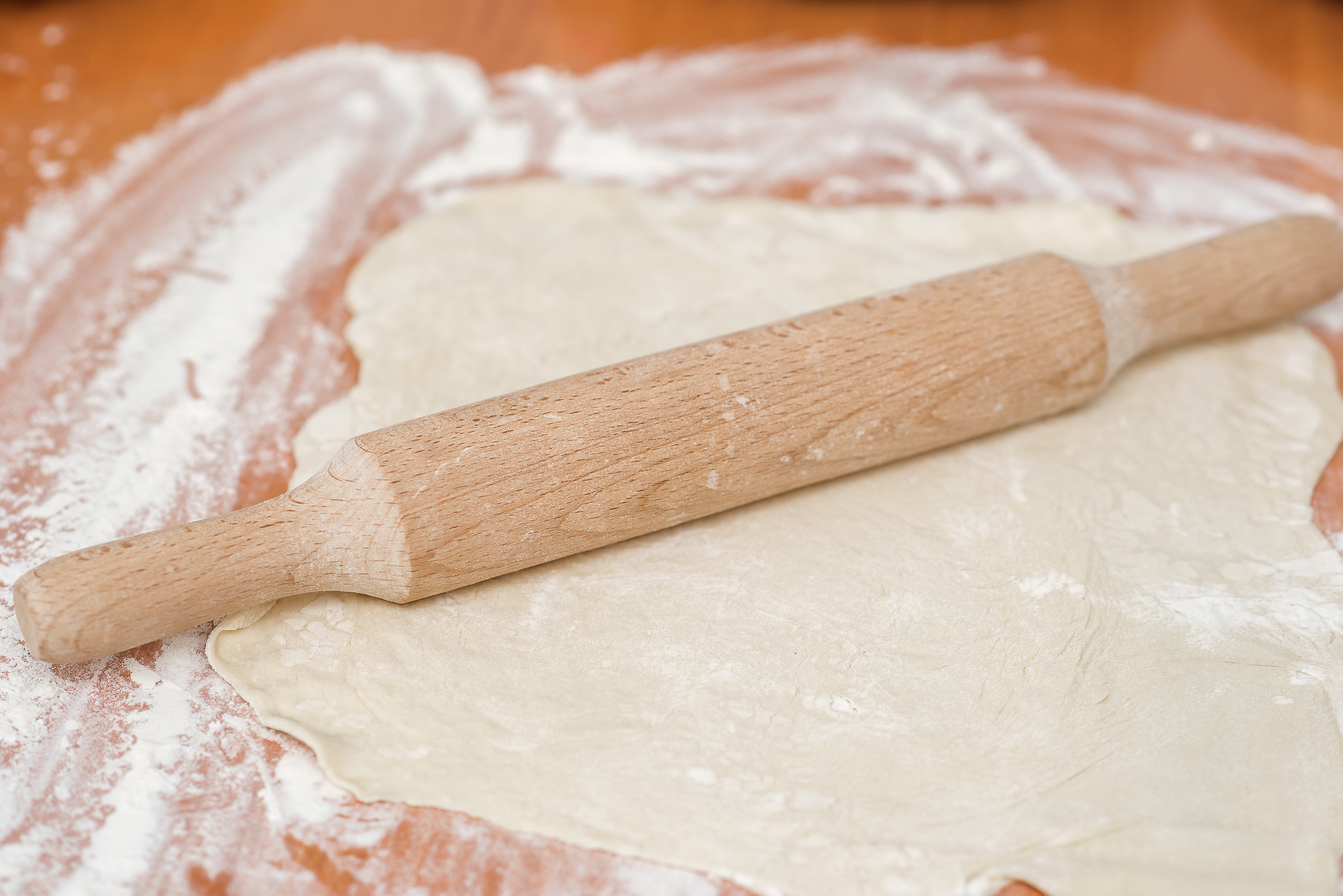 A wooden rolling pin rolls the dough sprinkled with flour.